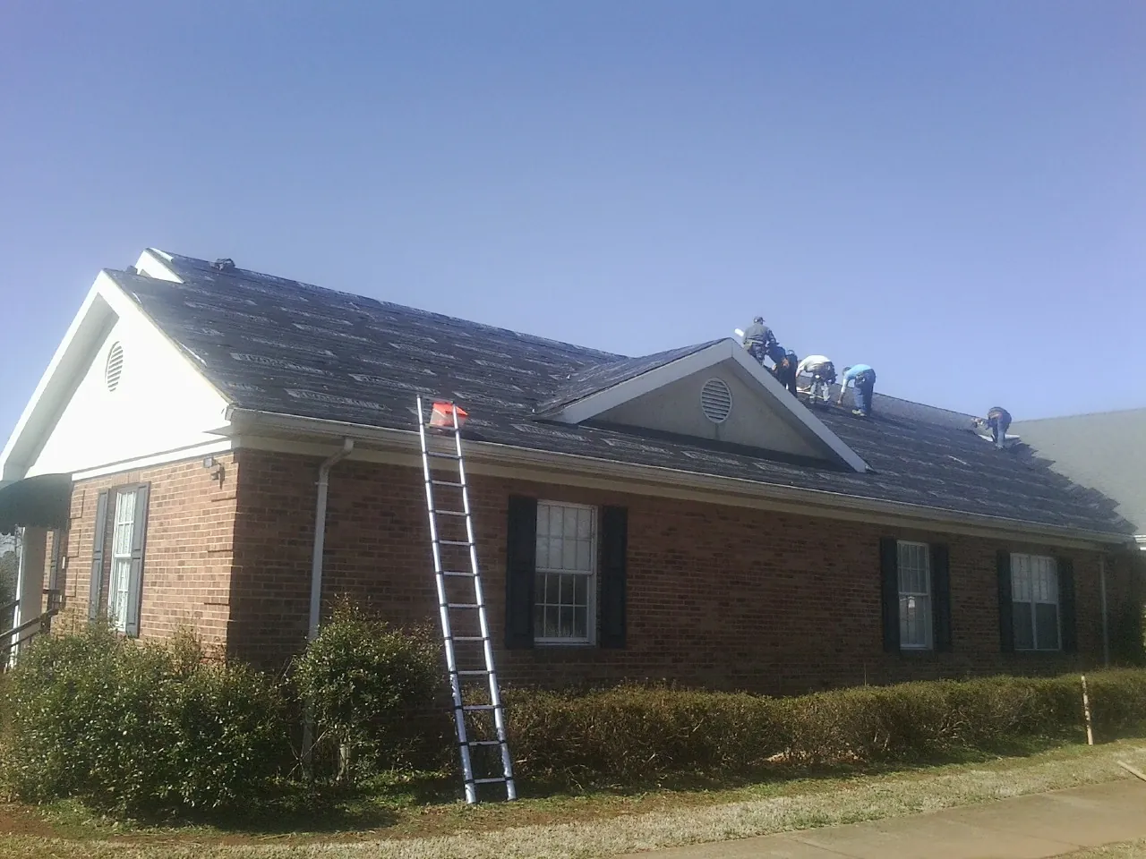 Crew tearing shingles off a brick ranch roof with a ladder set — Emergency Roof Repair work by our crew in Sandwich