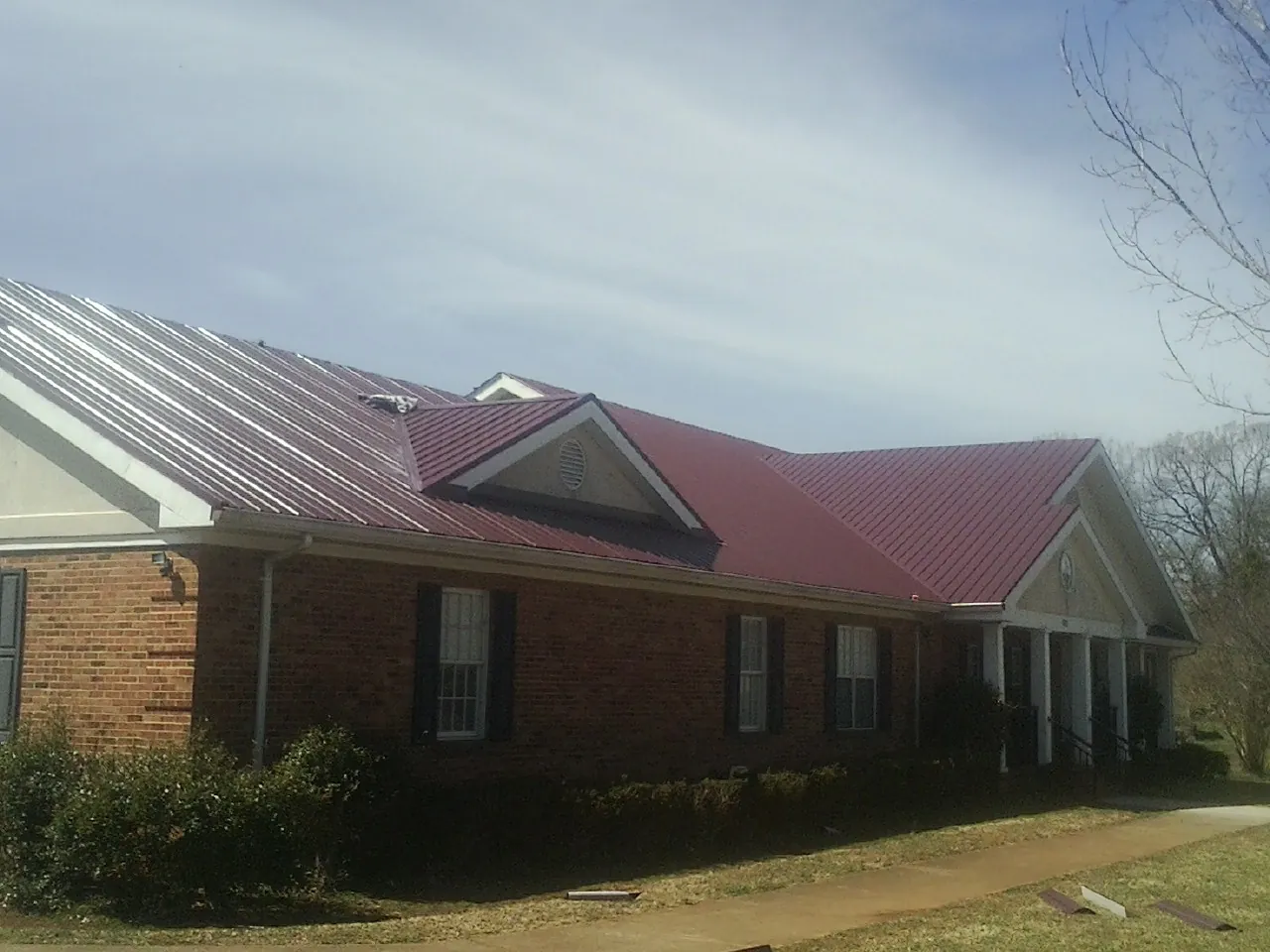 Red metal roof with gabled entries on a long brick building, from a Hail Damage Roof Repair job in Sandwich